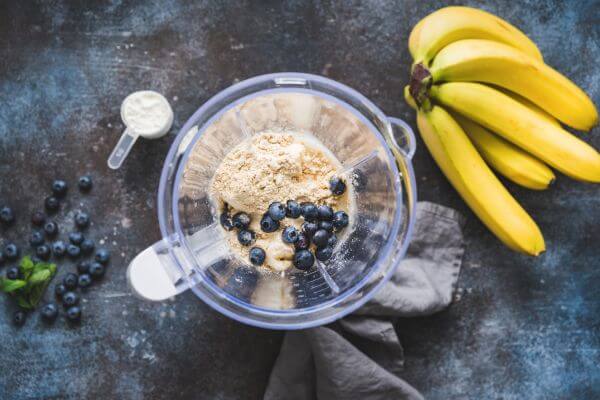 a blender with blueberries and protein powder and whole bananas