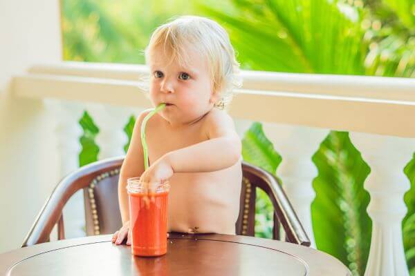 a 3yr old toddler drinking a smoothie and putting their hand in the glass